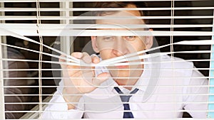 Man in a white shirt and tie sits at a window with blinds. The room is hot and stuffy