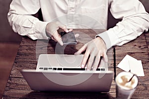 Man in white shirt working on portable computer and drinking latte in a cafe or coworking. Focus on guy`s hand and keyboard