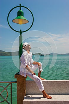 The man  in a white suit and hat sitting on a rock on the sea ba