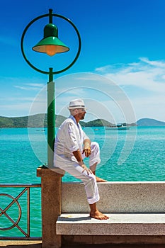 The man in a white suit and hat sitting on a rock on the sea ba