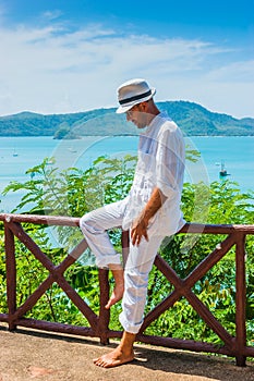 The man in a white suit and hat sitting on a rock on the sea ba