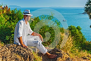 The man in a white suit and hat sitting on a rock on the sea ba