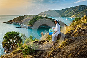 The man in a white suit and hat sitting on a rock on the sea ba