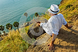 The man in a white suit and hat sitting on a rock on the sea ba