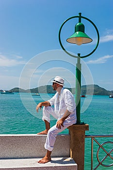 The man in a white suit and hat sitting on a rock on the sea ba