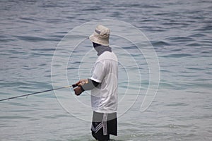 a man in a white t-shirt and black shorts is fishing on the beach in Lombok