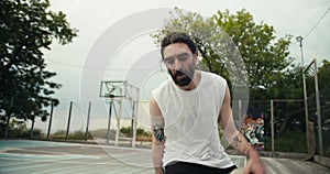 A man in a white t-shirt and black shorts skillfully dribbles a basketball on a basketball court outside in summer