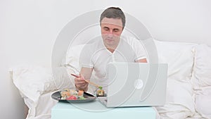 man in white t-shirt eating sushi in bed dipping sushi work online freelancer food delivery asian cuisine healthy food
