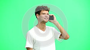 A man in a white T-shirt, on a green background, close-up, with a phone