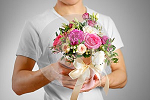 Man in white t shirt holding in hand rich gift bouquet. Composition of flowers in a pink hatbox. Tied with wide white ribbon and