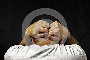 A man in a white T-shirt holds his hands behind his head. Closeup on black background.