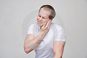 A man with a white T-shirt massages his ear in pain.