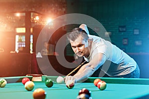 A man in a white T-shirt is playing billiards, a dark background. Pleasant pastime, entertainment, leisure, family holidays, games