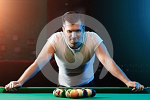 A man in a white T-shirt is playing billiards, a dark background. Pleasant pastime, entertainment, leisure, family holidays, games