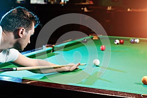 A man in a white T-shirt is playing billiards, a dark background. Pleasant pastime, entertainment, leisure, family holidays, games