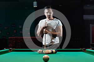 A man in a white T-shirt is playing billiards, a dark background. Pleasant pastime, entertainment, leisure, family holidays, games