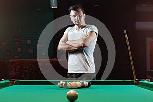 A man in a white T-shirt is playing billiards, a dark background. Pleasant pastime, entertainment, leisure, family holidays, games