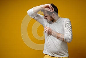 Man in a white t-shirt sniffs his armpits, annoyed by the problem of foul perspiration and body stench. Copy space. photo