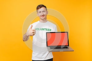 Man in white t-shirt written inscription green title volunteer hold laptop pc computer with blank empty screen isolated