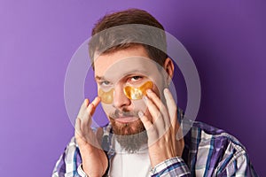 Man in white tshirt with eye patches stand against violet background. Beauty treatment spa wellbeing concept