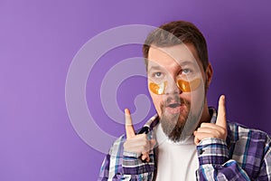 Man in white tshirt with eye patches stand against violet background. Beauty treatment spa wellbeing concept