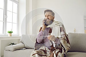 Man who has flu and fever sitting on couch and talking to his doctor on cellphone