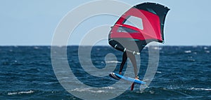 A man is wing foiling using handheld inflatable wings and hydrofoil surfboards in a blue ocean