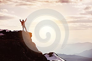 Man in winner pose at mountain top against mountains and sunset