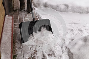 Man in winter boots  cleaning snow on walkway in garden with snow shovel.