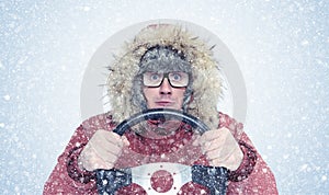 Man in winter clothes with a steering wheel, snow, blizzard. Concept car driver