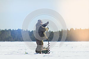 A man on a winter fishing drill hole ice drill