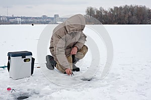 Man on winter fishing. The fisherman is on one knee and sets up a fishing rod. photo