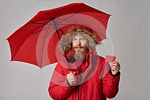 Man in winter jacket with umbrella showing blank credit card