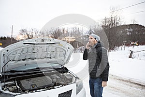Man on the winter road is calling the phone near the car