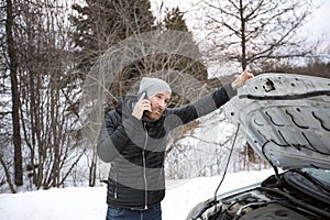 Man on the winter road is calling the phone near the car