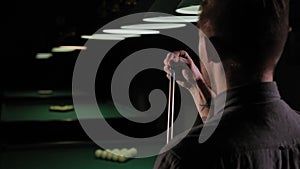 Man wipes a cue with chalk ready to start game. Pool room on the background.