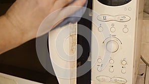 A man wipes the end of the microwave door with a damp cloth.Cleaning dirty microwave oven.