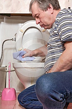 A man wipes the rim of a dirty toilet with a rag