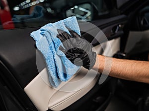 A man wipes the surface of the car interior with a microfiber cloth.