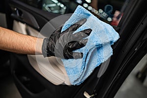 A man wipes the surface of the car interior with a microfiber cloth.