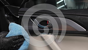 A man wipes the surface of the car interior with a microfiber cloth.