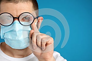 Man wiping foggy glasses caused by wearing disposable mask on background, space for text. Protective measure during