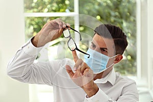 Man wiping foggy glasses caused by wearing medical mask indoors