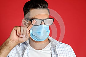 Man wiping foggy glasses caused by wearing medical mask on red background