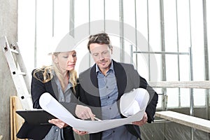 Man and woman architects or engineers work together discussing with blueprint in the inside the construction building site