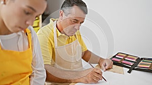 Man and woman artists, deep in concentration, sitting together in art studio drawing on a notebook