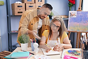 Man and woman artists smiling confident drawing on notebook at art studio