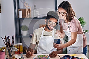 Man and woman artists using smartphone drawing on notebook at art studio