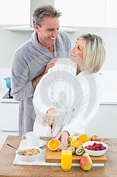 Man with a woman as she cuts fruits in kitchen