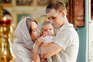 man and woman with baby son in light-colored robes by window in church.